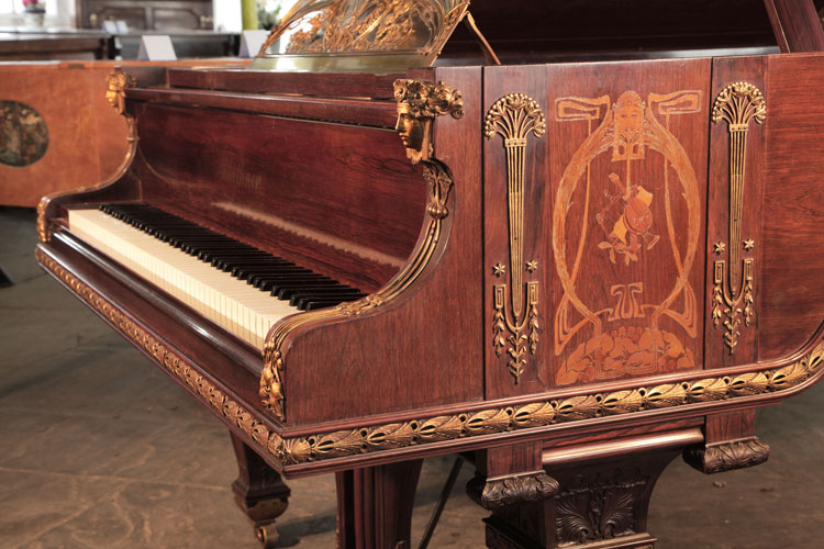 The piano cheek side panel is inlaid with an Art Nouveau design featuring a stylised female head surrounded by whiplash lines and foliage. Musical instruments sit centrally in the design. Columnar, Empire style gilt mounts stand each side of the inlay. Napoleonic emblems of stars, palmettes and foliage feature here. Symmetrical female heads with flowing tresses and floral headbands in gilt metal sit atop each cheek with flowing tendrils leading to stylised foliage