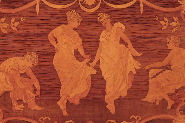 Steinway inlay of dancing ladies in voluminous gowns flanked by seated male figures