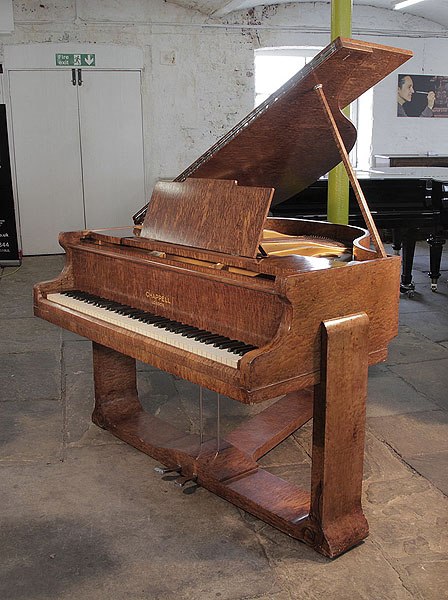 A 1936, Art Deco style, Chappell baby grand piano for sale with a quilted maple case. Cabinet features sculptural piano legs attached to a cross stretcher. Piano pedals integrated into cross stretcher. 