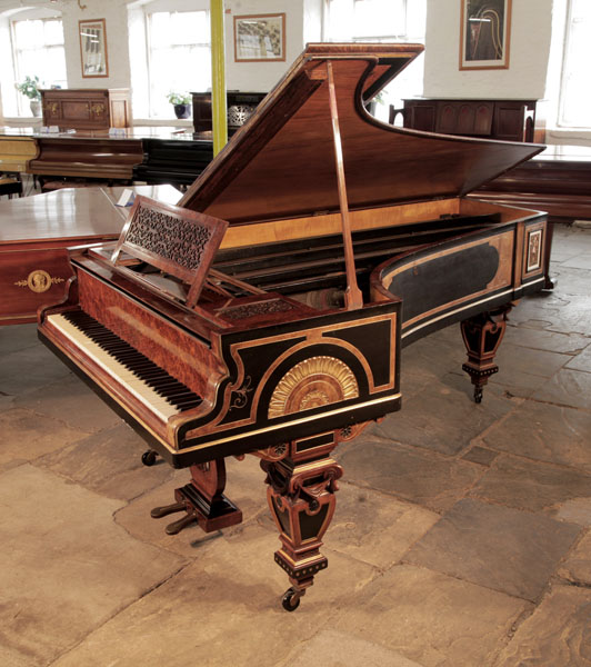 An 1861, Erard grand piano with an ornate burr walnut, black and gilt cabinet. Piano casework features Egyptian Revival and Neoclassical elements..