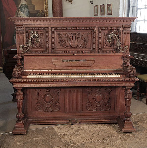 Antique, Georg Fortner upright piano for sale with an ornately carved, mahogany case and ornate candlesticks. Cabinet features carved flowers, foliage, musical instruments and grotesque heads on each piano cheek